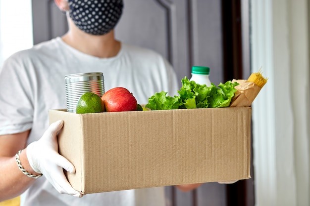 Volunteer in the protective medical mask and gloves delivery donation box at home