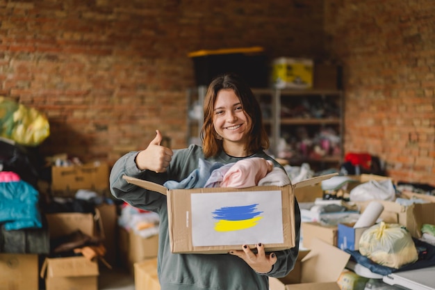 Volunteer teengirl preparing donation boxes for people in need in Ukraine Donation clothing for refugees from Ukraine support of war victims a box with the Ukrainian flagHumanitarian aid concept