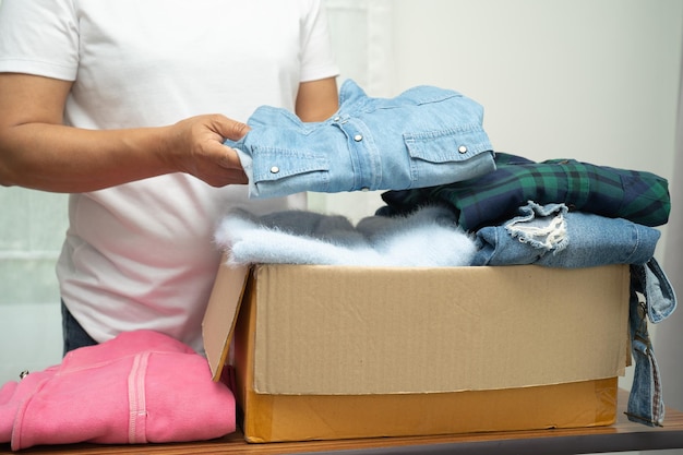 Volunteer woman holding clothing donation box with used clothes at home to support help for poor people in the world