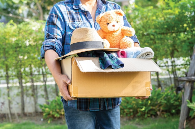 Volunteer woman provide clothing donation box with used clothes and doll to support help for refugee homeless or poor people in the world