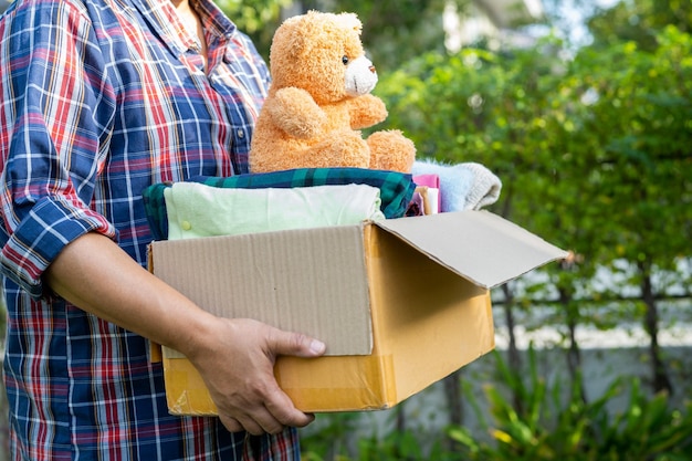 Volunteer woman provide clothing donation box with used clothes and doll to support help for refugee homeless or poor people in the world