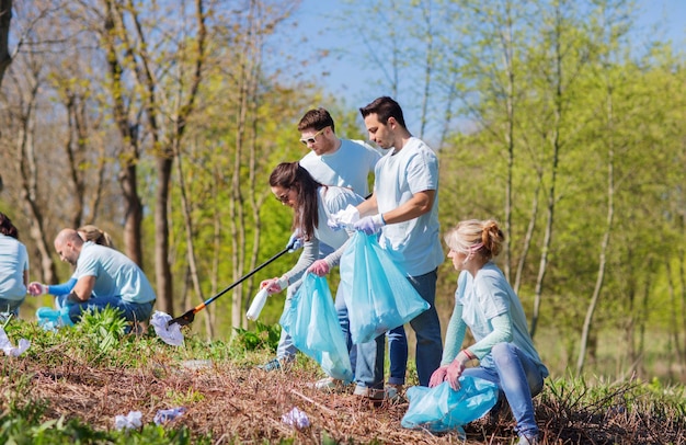 volunteering, charity, cleaning, people and ecology concept - group of happy volunteers with garbage bags cleaning area in park