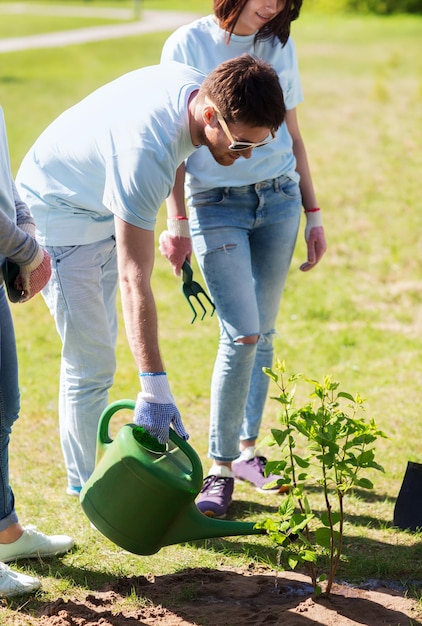 volunteering, charity, people and ecology concept - group of happy volunteers planting and watering tree with can in park