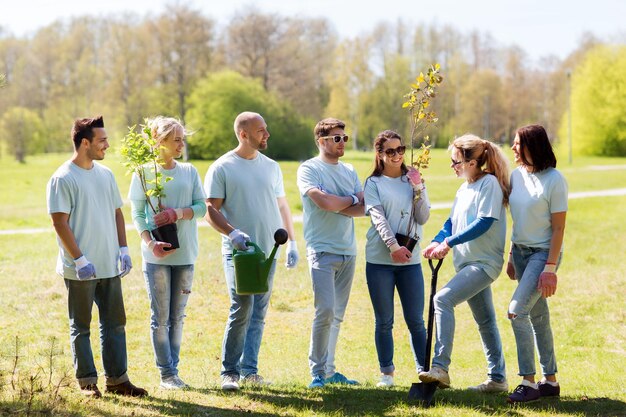 volunteering, charity, people and ecology concept - group of happy volunteers with tree seedlings and gardening tools in park