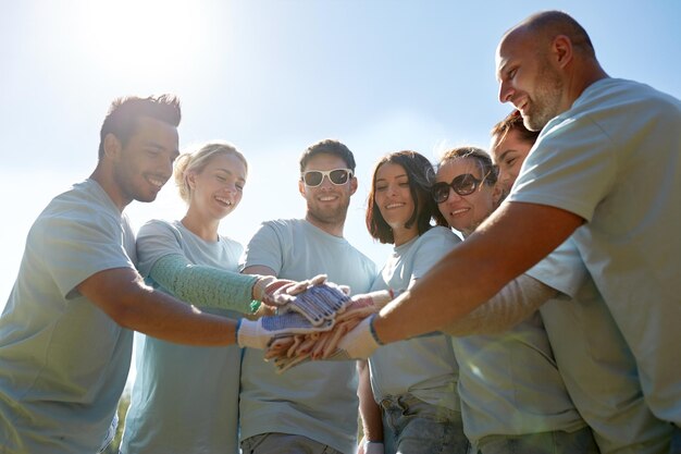 Photo volunteering, charity, people, gesture and ecology concept - group of volunteers putting hands on top outdoors