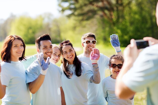 ボランティア、チャリティー、人、チームワーク、環境のコンセプト – 公園でスマートフォンで写真を撮る幸せなボランティアのグループ