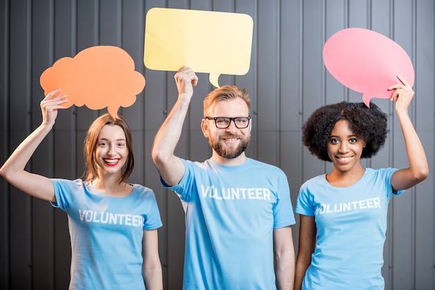 Volunteers holding colorful thought bubbles standing on the gray wall background