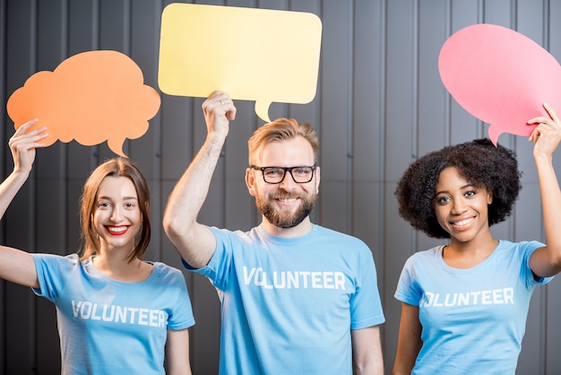 Volunteers holding colorful thought bubbles standing on the gray wall background