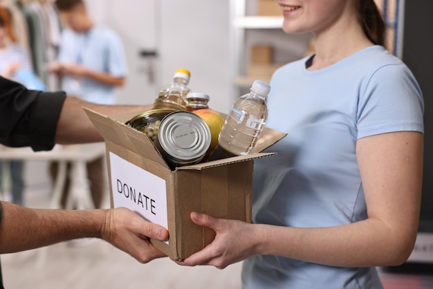Volunteers holding donation box with food products indoors closeup