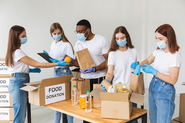 Volontari con guanti e maschere mediche che preparano il cibo per la donazione