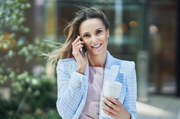 Volwassen aantrekkelijke zakenvrouw met smartphone en koffie wandelen in de stad. hoge kwaliteit foto