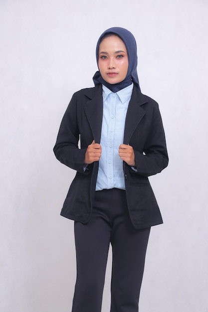 Volwassen Aziatische kantoorvrouw met een hijab blauw hemd die met een elegante glimlach staat en haar jack vasthoudt