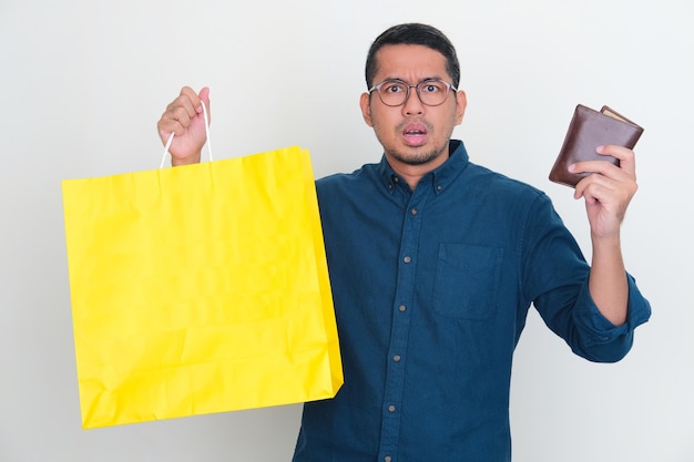Volwassen Aziatische man die een bezorgde uitdrukking toont terwijl hij een boodschappentas en portemonnee vasthoudt
