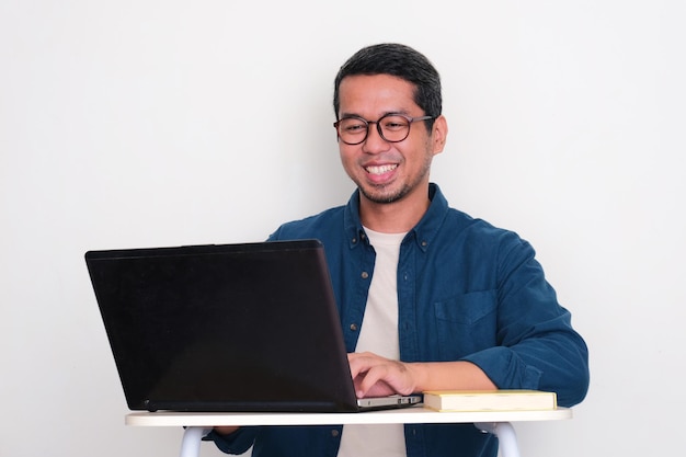 Volwassen Aziatische man die gelukkig glimlacht als hij met een laptop werkt