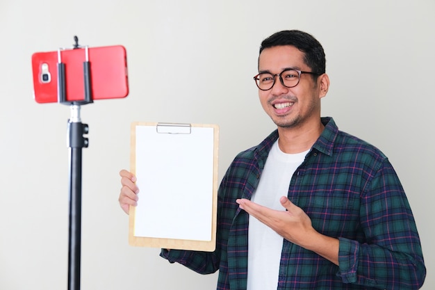 Volwassen Aziatische man die lacht terwijl hij leeg wit papier presenteert tijdens een conferentie voor mobiele telefoongesprekken