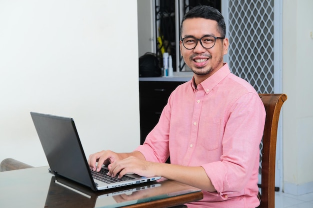 Volwassen Aziatische man die lacht tijdens het werken met een laptop in zijn huis