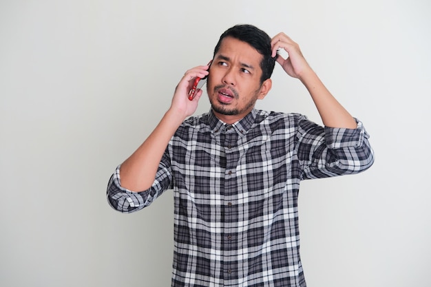Volwassen Aziatische man die verwarde uitdrukking toont terwijl hij met iemand aan de telefoon praat