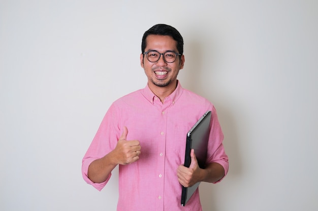 Volwassen Aziatische man die zelfverzekerd glimlacht terwijl hij een laptop vasthoudt en zijn duim opgeeft