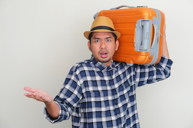 Volwassen Aziatische man draagt een bagage en toont een verwarde uitdrukking