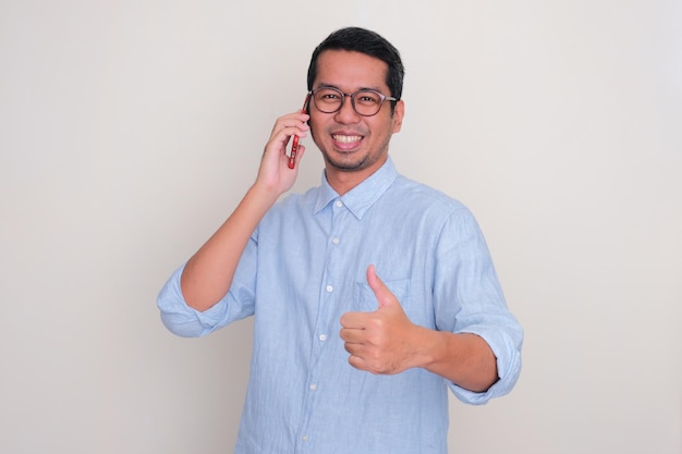 Volwassen Aziatische man glimlachend en duim omhoog terwijl hij belt met zijn mobiele telefoon