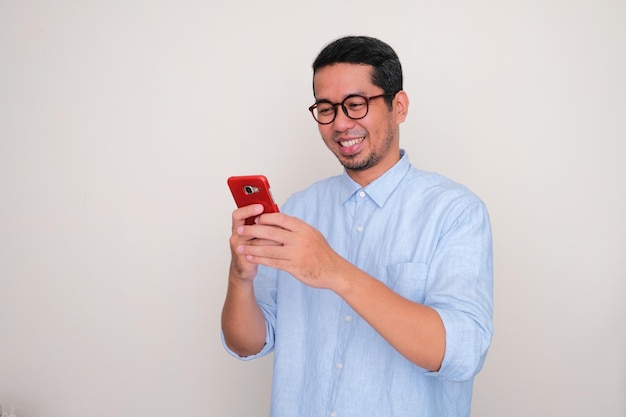 Volwassen Aziatische man glimlachend gelukkig bij het typen op zijn mobiele telefoon