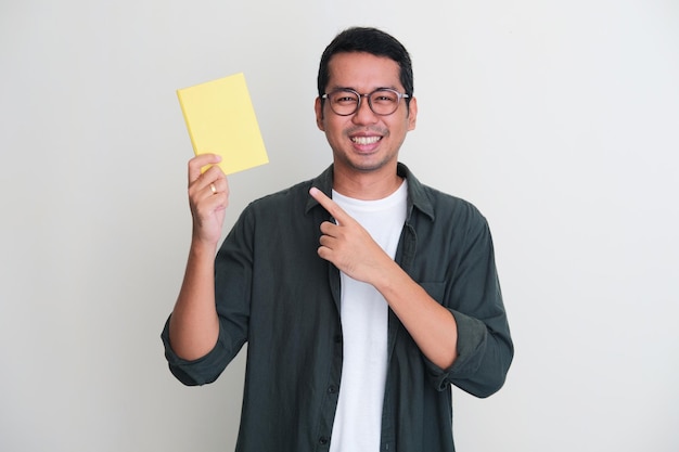 Volwassen Aziatische man lacht blij naar de camera terwijl hij wijst naar het boek dat hij vasthoudt