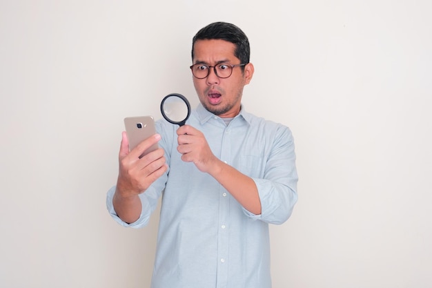 Foto volwassen aziatische man vindt iets in zijn mobiele telefoon met behulp van een vergrootglas