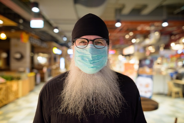 Volwassen bebaarde hipster man met masker voor bescherming tegen corona virus uitbraak in het winkelcentrum