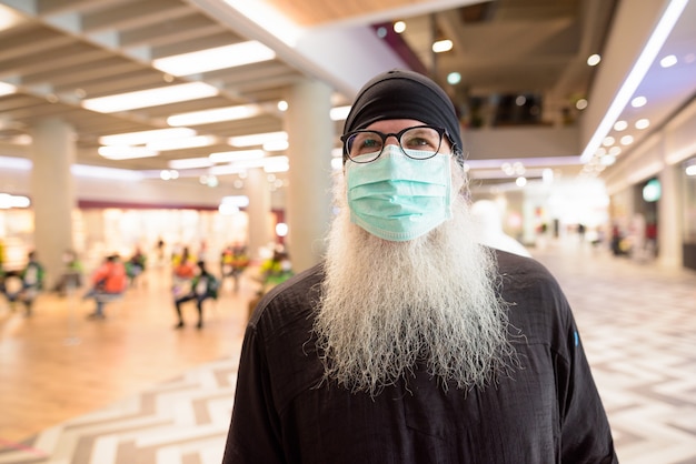 Volwassen bebaarde hipster man met masker voor bescherming tegen corona virus uitbraak winkelen met afstand in het winkelcentrum