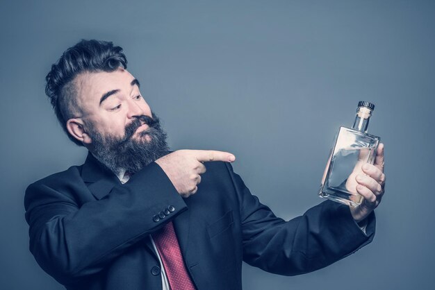 Foto volwassen bebaarde man in pak wijzend op een fles alcohol in de hand