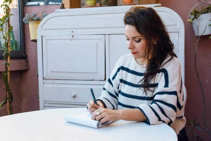 volwassen blanke vrouw die alleen thuis zit te schetsen met een zwarte stift op basis van een wit blok