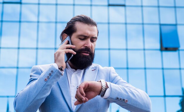 Volwassen brutale man spreken aan de telefoon in formele kleding modieuze bebaarde hipster dragen jas zelfverzekerde en charismatische man met baard en snor buiten mannelijke stedelijke mode zakelijke communicatie