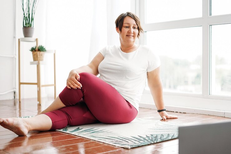 Volwassen charmante brunette vrouw plus size body positive oefent thuis yoga met laptop