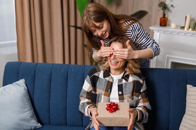 Volwassen dochter feliciteert moeder die haar ogen bedekt en een geschenkdoos geeft