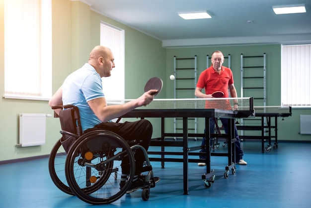 Volwassen gehandicapte man in een rolstoel speelt tafeltennis met zijn coach