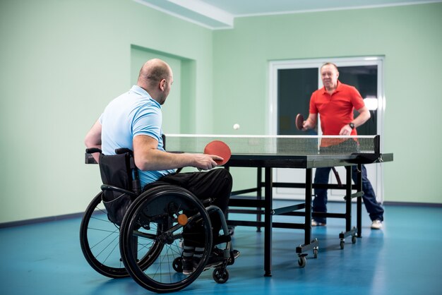 Volwassen gehandicapte man in een rolstoel speelt tafeltennis met zijn coach