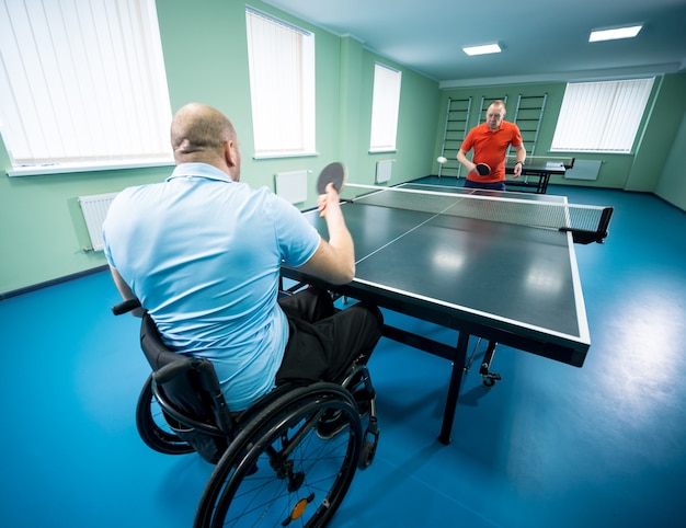 Volwassen gehandicapte man in een rolstoel speelt tafeltennis met zijn coach