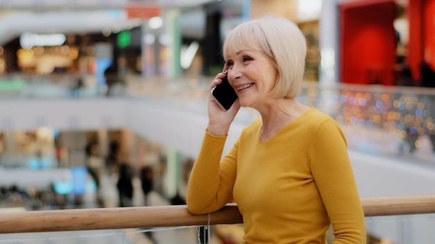 Volwassen gelukkige vrouw spreekt vriendelijk aan de telefoon, beantwoordt telefoontjes, communiceert met familie met behulp van een smartphone