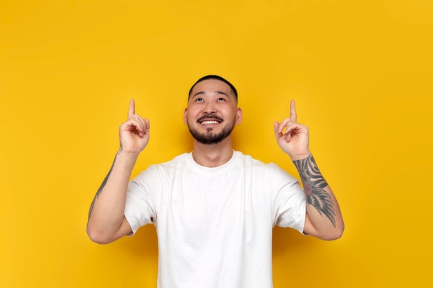 volwassen getatoeëerde Aziatische man in witte t-shirt toont zijn handen op gele geïsoleerde achtergrond