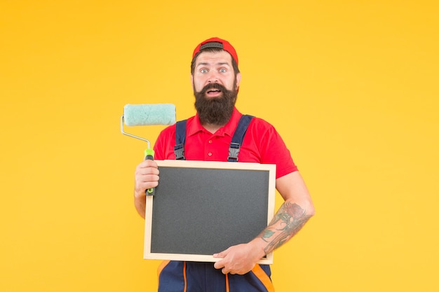 Volwassen hipster gebruik verfroller tool om te schilderen. reparateur of bouwer werken. creatief idee. voorman adverteert met de service van wandbekleding. verbaasde brutale man in overall met bord kopieerruimte.