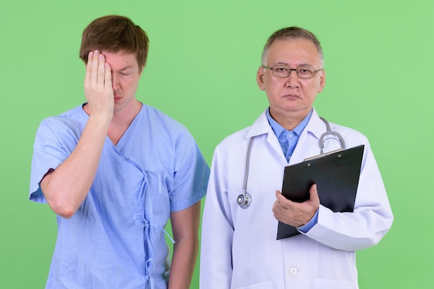 volwassen Japanse man arts en Scandinavische man patiënt samen tegen chroma key met groene muur