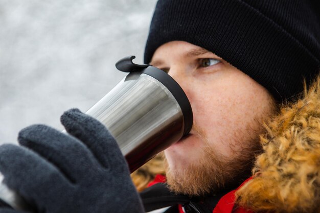 Foto volwassen jonge man drinkt koffie uit een hervulbare beker buiten winter outfit