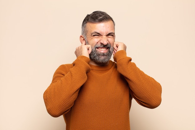 Foto volwassen knappe man die boos, gestrest en geïrriteerd kijkt en beide oren bedekt met een oorverdovend geluid, geluid of luide muziek