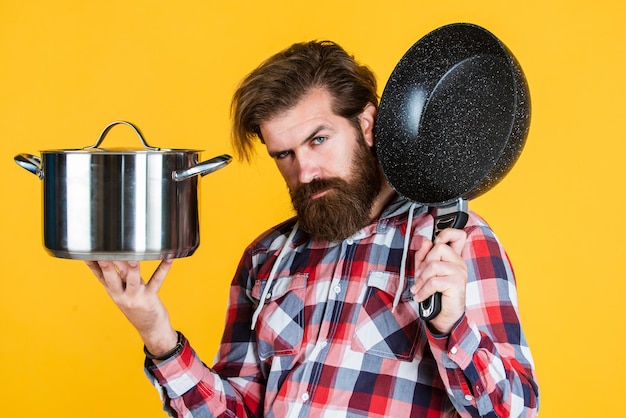 Volwassen knappe man in geruit hemd houdt pan vast voor het koken van voedsel, technologie.
