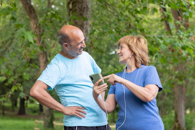 Volwassen koppel lacht om een foto op hun smartphone terwijl ze uitrusten van het sporten in het stadspark