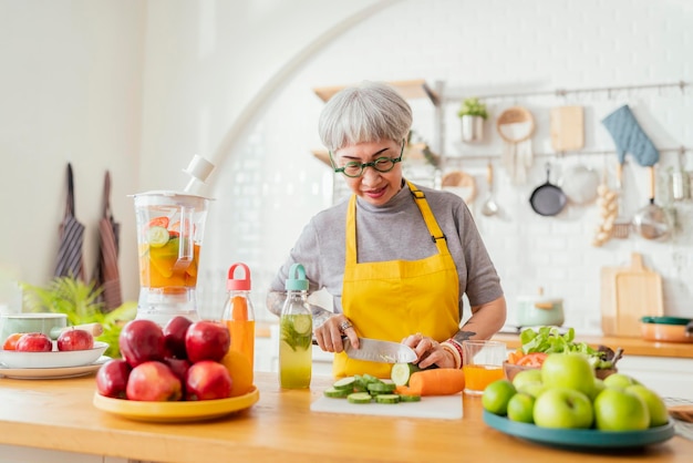 Volwassen lachende tattoo vrouw salade groenten en fruit eten Aantrekkelijke volwassen vrouw met verse groene fruitsalade thuis Senior vrouw schort staande in het aanrecht ontspannen in huis