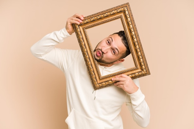 Volwassen Latijnse man die een vintage frame vasthoudt en geïsoleerd glimlacht