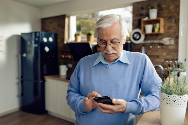 Volwassen man die mobiele telefoon gebruikt en sms leest terwijl hij in de keuken staat