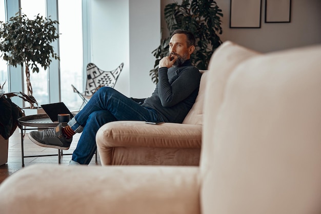 Volwassen man geniet van het uitzicht vanuit het raam van het appartement