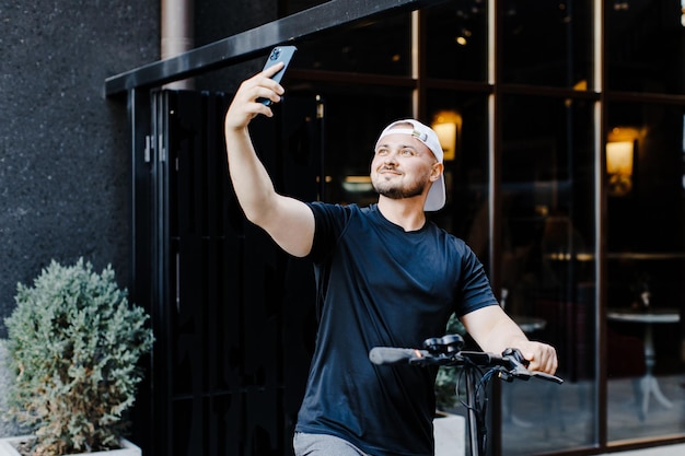 Volwassen man goed gekleed met elektrische scooter die een selfie maakt met zijn mobiele telefoon op straat